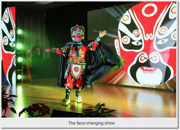 A masked face-changing performer in a colourful costume on a theatre stage