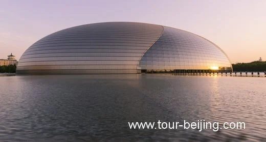 The curved National Centre for the Performing Arts reflected in its surrounding pool at sunset